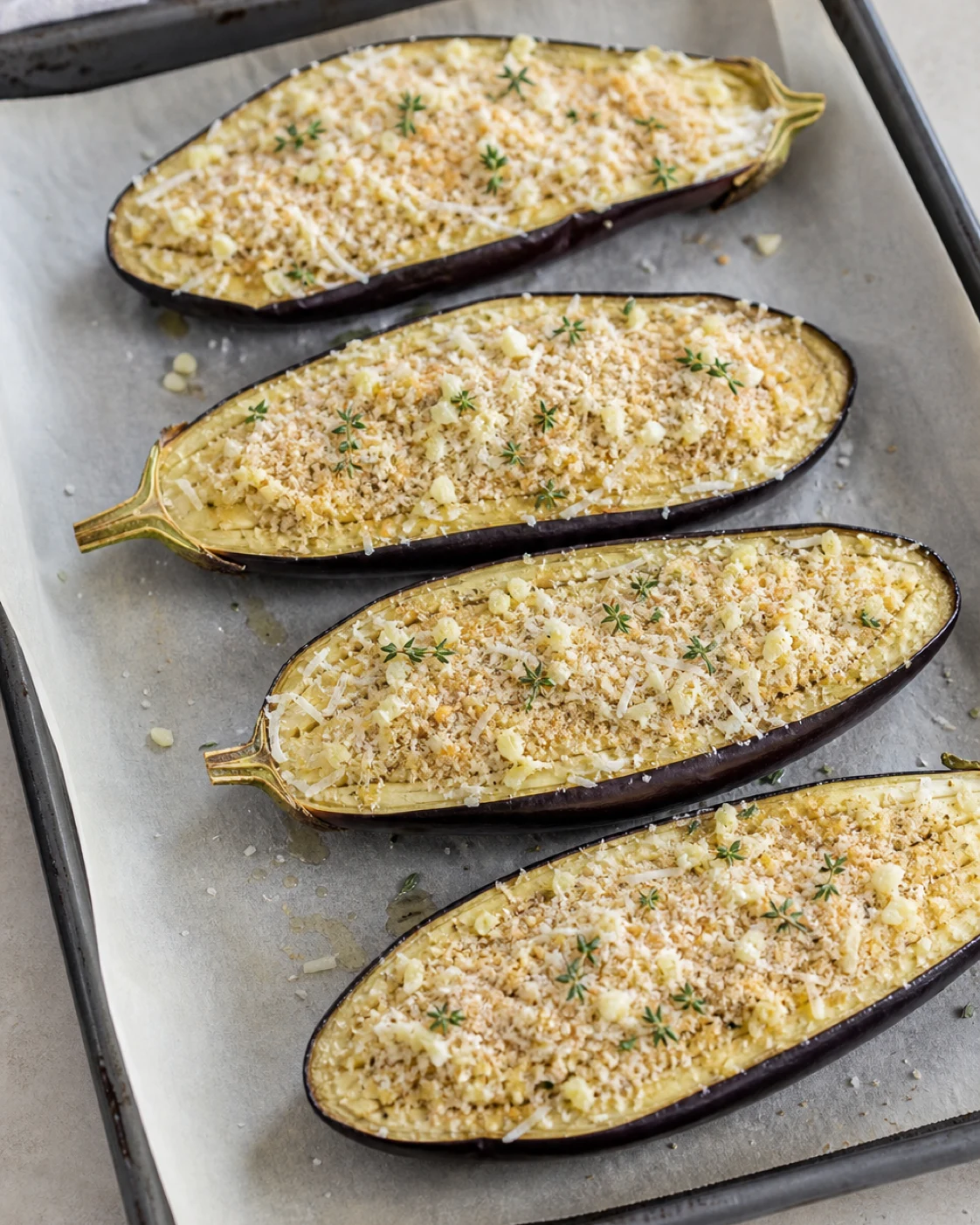 Demi-aubergines retournées sur une plaque avec ail, parmesan et chapelure avant la finition au four