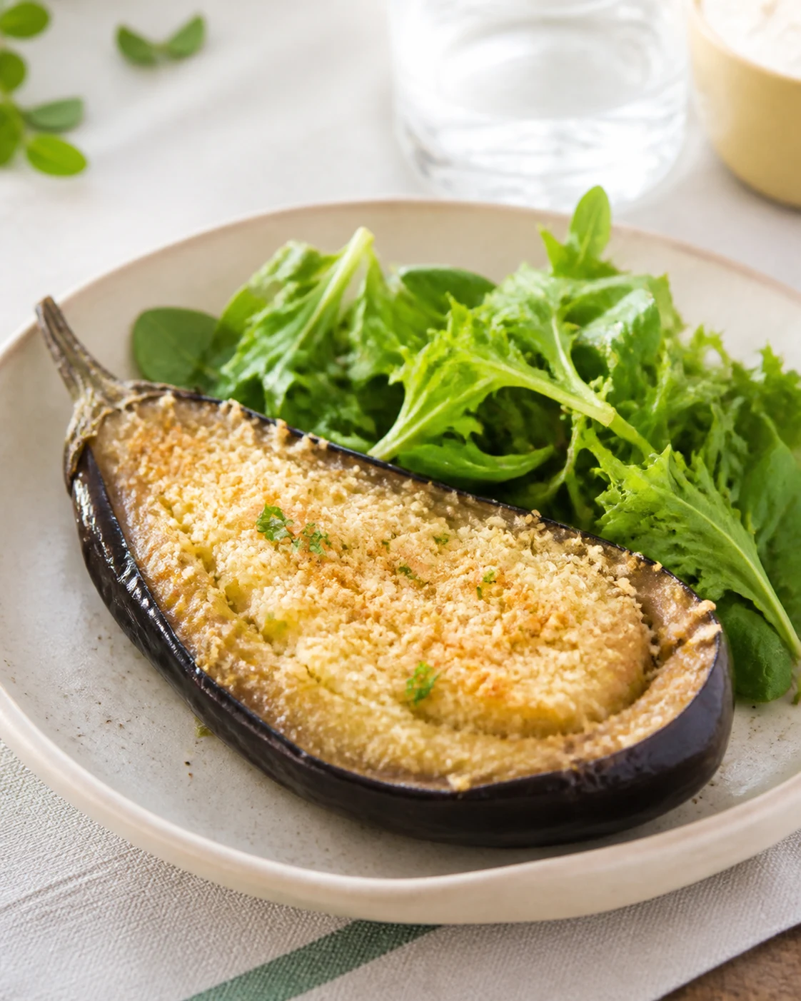 Une demi-aubergine au four au parmesan servie dans une assiette claire avec salade verte