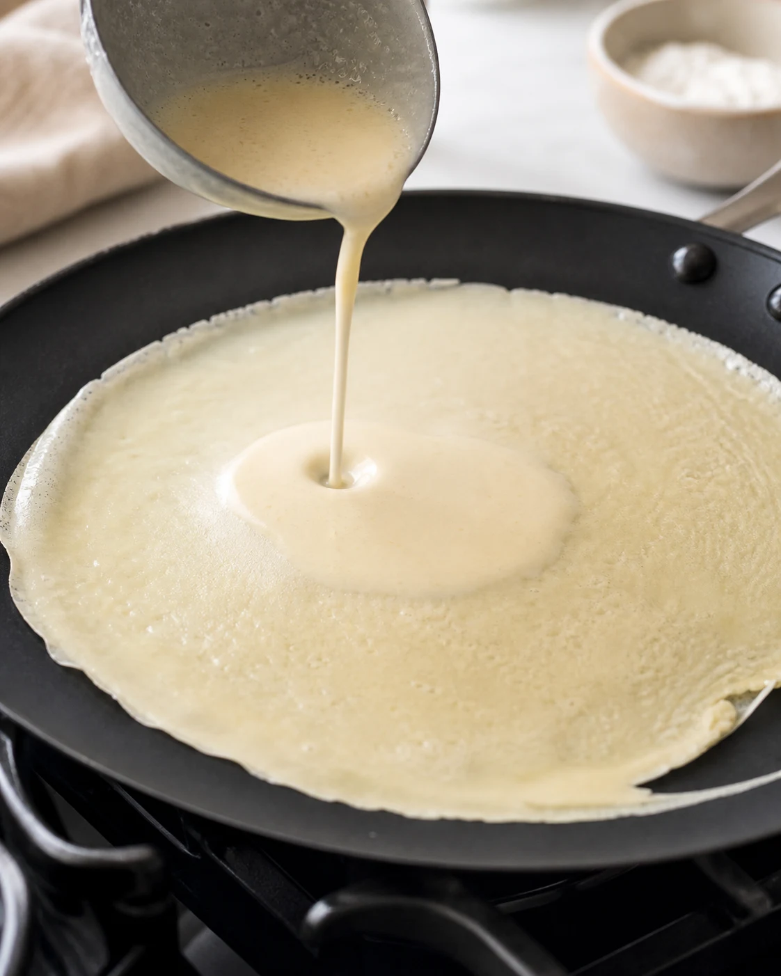 Pâte à crêpes sans gluten versée dans une poêle chaude avec bords qui commencent à prendre