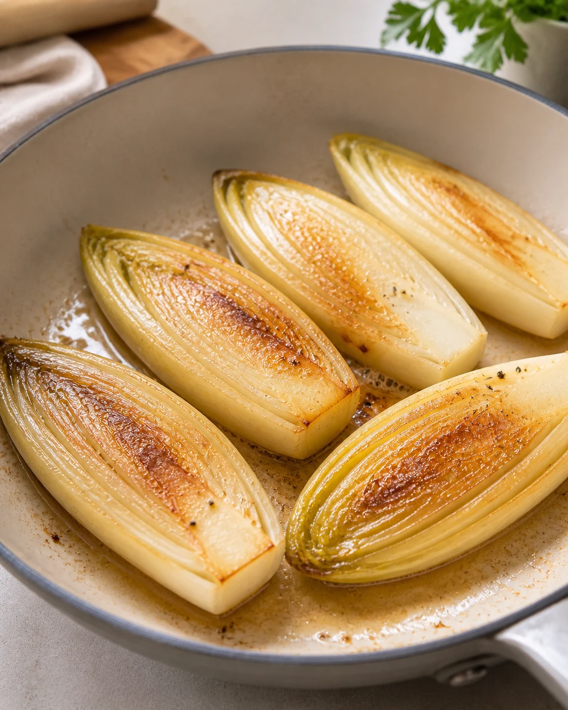 Demi-endives en train de dorer cote plat dans une sauteuse avec debut de caramelisation