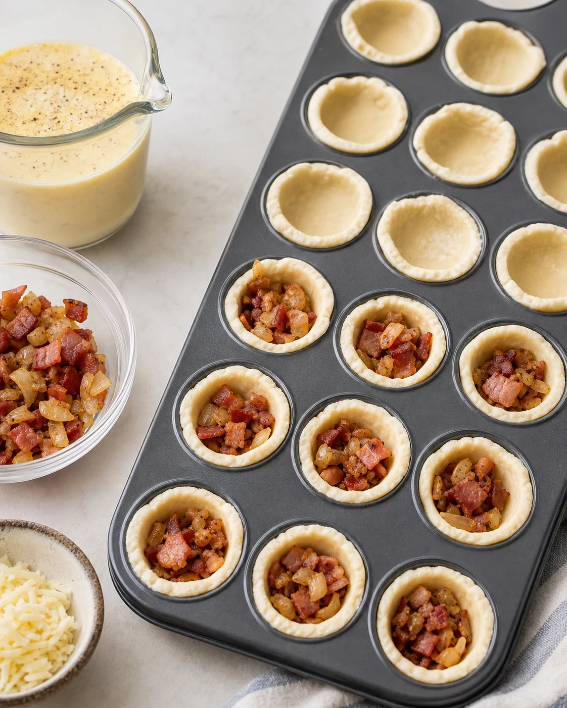 Preparation de mini quiches avec fonds de pate dans un moule mini muffins, garniture lardons oignon et appareil pret a etre verse
