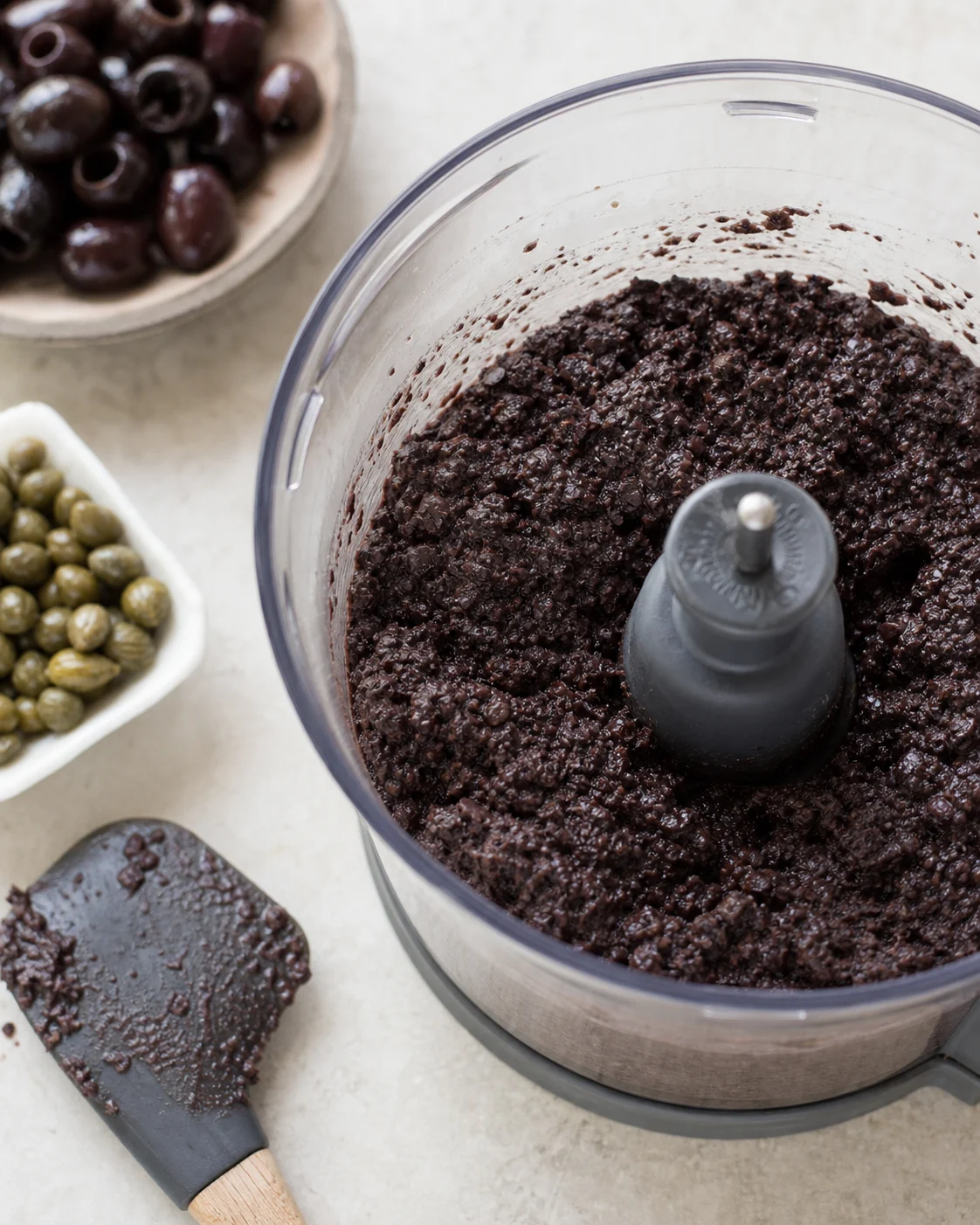 Préparation de tapenade noire maison avec texture épaisse et granuleuse dans un bol de mixeur